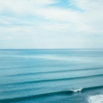 Perfect parallel ocean waves rolling toward shore under soft cloudy sky creating peaceful seascape